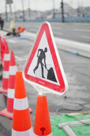 Mann läuft mit Verkehrszeichen auf Straße mit Baustelle.