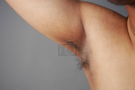 young man raised his hand up and showing his unshaven armpit .