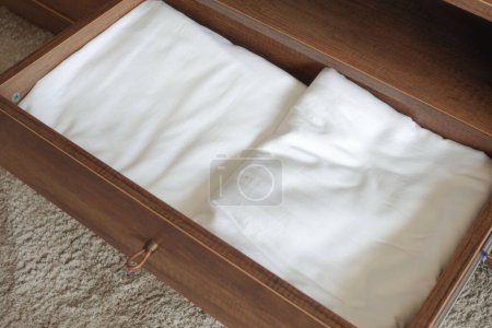 A rectangular wooden drawer on the floor contains two white linens. The hardwood plywood has a wood stain and varnish, with a patterned design