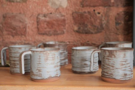 Tableware mugs displayed on hardwood shelf against brick wall.