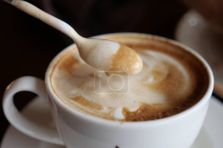 Savor a steaming cappuccino with frothy foam swirled in a cup, generating a warm aroma in a cozy cafe ambiance