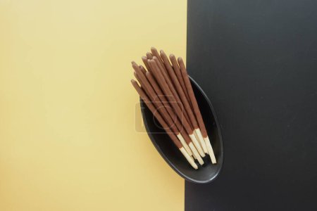 Chocolate dipped biscuit sticks in a black bowl arranged on a striking yellow and black background.