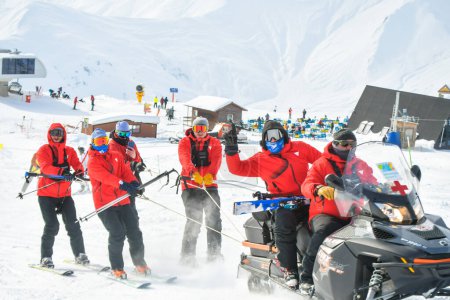 Foto de Gudauri, Georgia - 15 de febrero de 2022: el equipo de rescate de esquí en la estación de esquí de invierno disfruta del trabajo y diviértete. Equipo de rescate de motos de nieve al aire libre - Imagen libre de derechos
