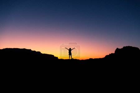 Téléchargez les photos : Heureuse de célébrer le succès gagnant femme au coucher du soleil ou au lever du soleil debout exalté avec les bras levés dans la célébration d'avoir atteint l'objectif du sommet de la montagne pendant la randonnée trek - en image libre de droit