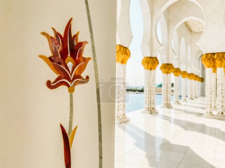 Foto de Abu dhabi, Emiratos Árabes Unidos - 3 de octubre de 2022: cerrar las flores en las columnas de arte detalles exteriores en la Gran mezquita. Corredores de la Gran Mezquita con nadie a la luz del sol - Imagen libre de derechos