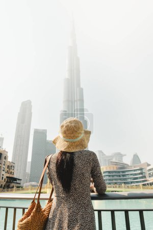Dubai, Emiratos Árabes Unidos - 11 de octubre de 2022: Viajera turista moderna que mira la torre Burj Khalifa contra el cielo blanco brumoso, Dubai, Emiratos Árabes Unidos