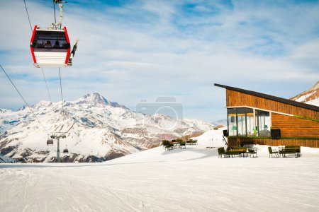 Photo for White red closed ski lift cabin with skiers and white dramatic snowy mountains background. Ski resort reopens. Georgia winter holidays in Gudaur. Kobi slopes cafe and area - Royalty Free Image