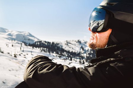 Téléchargez les photos : Close up of the ski goggles of caucasian man with the reflection of snowed mountains and sunburst. A mountain range reflected in the ski mask. Portrait of man at the ski resort - en image libre de droit
