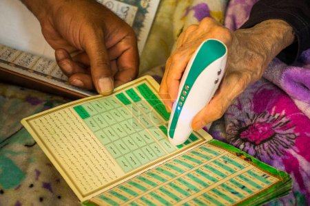 Photo for YAzd, Iran - 22nd june, 2022: Elderly woman at home use electric Koran read pen to read in arabic - Royalty Free Image