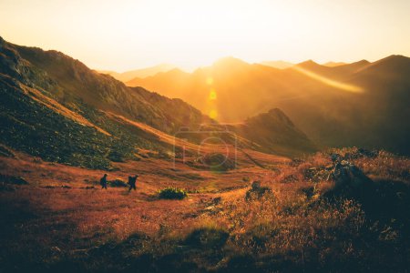 Foto de Dos amigos excursionistas en la distancia trekking lado izquierdo en el sendero al aire libre en la hermosa puesta de sol en otoño juntos. Personas activas en caminata en las montañas del Cáucaso - Imagen libre de derechos