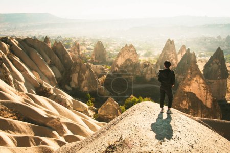 Photo for Thoughtful Female person stand look over dramatic valley on hazy morning sunrise with fairy chimneys background. Solo exploration in Turkey - Royalty Free Image