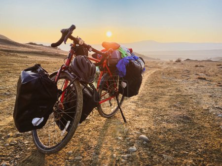 Téléchargez les photos : Chargé de sacs vélo rouge se trouve sur le côté de la route entourée de montagnes dans la campagne du parc national Vashlovani. Vacances à vélo en Géorgie - en image libre de droit