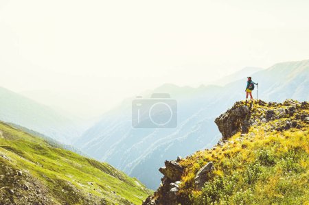 Foto de Vista trasera en forma de excursionista deportiva con bastones de paseo nórdicos se paran en el mirador cuesta arriba en el sendero de senderismo verde en las montañas del Cáucaso. Actividades recreativas y estilo de vida saludable. - Imagen libre de derechos