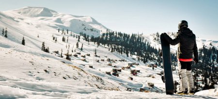 Téléchargez les photos : Homme snowboarder vêtu de noir foncé stand de vêtements de sport profiter d'un panorama du paysage de la station de ski sur la pente de montagne en Géorgie destination de vacances de ski - Goderdzi, Montagnes du Caucase - en image libre de droit