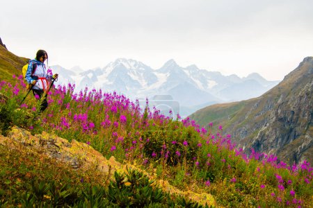 Seguimiento de vista lateral en forma de excursionista deportiva femenina con sondeos a pie nórdicos en el mirador cuesta arriba en sendero de senderismo verde en las montañas del Cáucaso. Actividades recreativas y estilo de vida saludable.