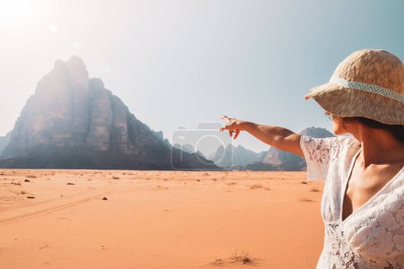 Back view female tourist stand watch point finger to seven pillars of wisdom monument in wadi rum desert-famous nature reserve in middle east. Explore Jordan banner