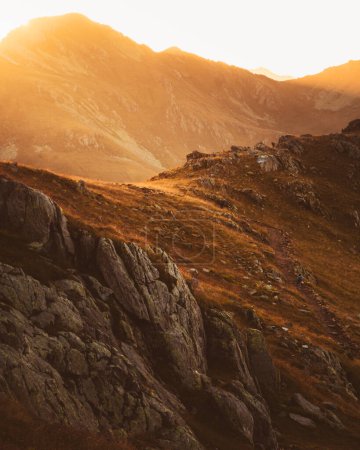 Foto de Mochilero de senderismo de seguimiento estático en pista de roca negra en Lagodekhi disfruta de una dramática puesta de sol sobre la montaña contra el sol - Imagen libre de derechos