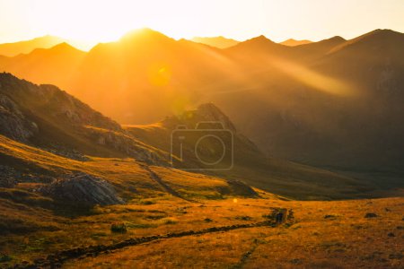 Foto de Panorama de la puesta del sol y el hombre senderistas mujer en caminata a distancia en el sendero al aire libre en la hermosa puesta del sol en otoño juntos. Caminata en cámara lenta contra la gente activa del sol en las montañas del Cáucaso - Imagen libre de derechos