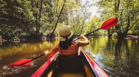 Back Rear View strong caucasian woman rowing Kayaking In Beautiful Lithuania countryside river - Zemeina. Action Camera POV Of Girl Paddling On canoe. Active holidays fun outdoors