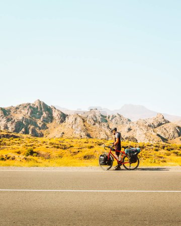 Solo ciclista en carretera con bicicleta comprobar mapa que se pierde al aire libre en el día soleado caliente en el desierto. El ciclista deportivo revisa el teléfono al costado de la carretera. Fondo vertical