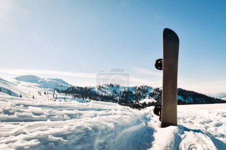 Snowboard avec bandes noires et blanches debout dans la neige avec des montagnes d'hiver en arrière-plan

