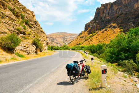 Beladen mit Taschen stehen rote Fahrradständer am Straßenrand, umgeben von Landschaft in Armenien, Kaukasusbergen. Radtourenurlaub.