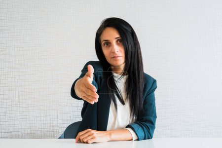 Jeune femme d'affaires brune caucasienne directrice dans le bureau derrière le bureau donner main pour poignée de main du point de vue du personnel des clients point de vue dans le bureau de patron employé