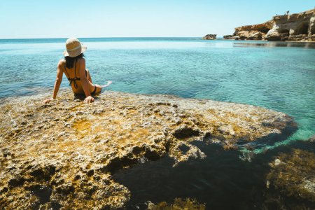 Belle femme caucasienne assis sur le point de vue rocher profiter des eaux cristallines et panorama du paysage marin méditerranéen pendant les vacances d'été. Bonheur et voyage explorer concept