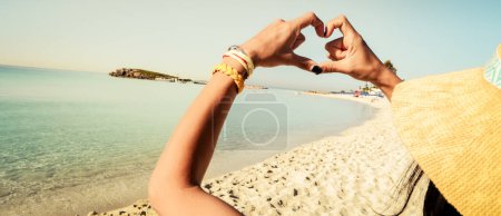 Happy girl tourist on sunny Nissi beach in Cyprus show Finger shaped heart shape sign. Hands of girl shape of heart. Summer dream. Happiness of freedom on holidays vacation