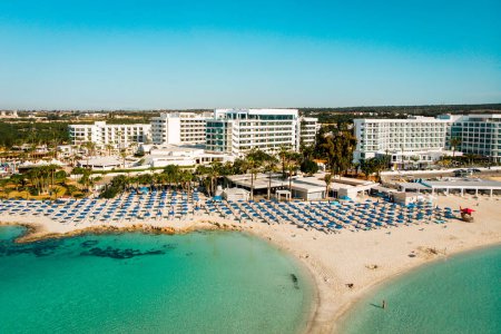 Ayia Napa, Cyprus - 15th april, 2023: aerial fly over Luxury hotel buildings with pools by beach with island greenery panorama.White sand most famous in Cyprus - Nissi beach