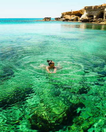 Mujer nada en la costa norte de la bahía de Ayia napa cyprus con aguas mediterráneas de color azul cristalino y un tranquilo paisaje marino y la costa de piedra rocosa. Cuevas marinas destino turístico popular