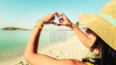 Happy girl tourist on sunny sandy Nissi beach in Cyprus show Finger shaped heart shape sign. Hands of girl shape of heart. Summer dream. Happiness of freedom on holidays vacation