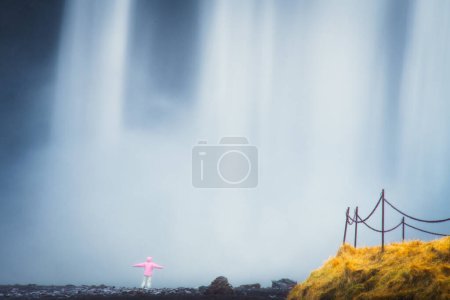 Vêtements touristiques veste rose stand par belle célèbre cascade Skogafoss en Islande au printemps