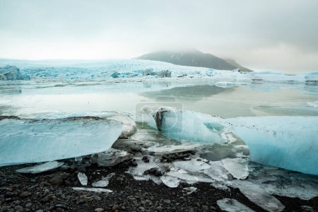 View of a blue iceberg broken off from the glacier tongue of Fjallsjkull in the glacier lagoon in Iceland on a cloudy day. With a view of