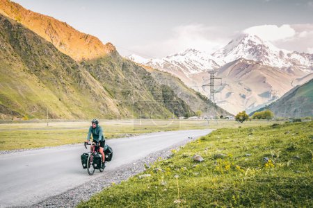 Caucasian male cyclist bicycle touring in caucasus KAzbegi mountains and Kazbek peak background. Travel around caucasus. Cycle around the world holidays outdoors