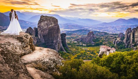 Caucasian greek wedding couple in elegant clothing on famous wedding photography spot on Meteora viewpoint during the sunset. Greek location wedding photography sessions concept