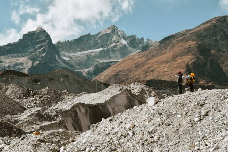 Dos excursionistas trekking en las montañas del Himalaya a través del glaciar Chola pasan a Gokyo Ri. Guía masculino nepalí que lidera el cliente turístico en la caminata oficial del parque nacional Sagarmatha.