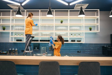 Téléchargez les photos : Nettoyeurs d'entreprise de nettoyage en cours de nettoyage général dans la zone de cuisine en coworking, ils sont en uniforme et gants - en image libre de droit