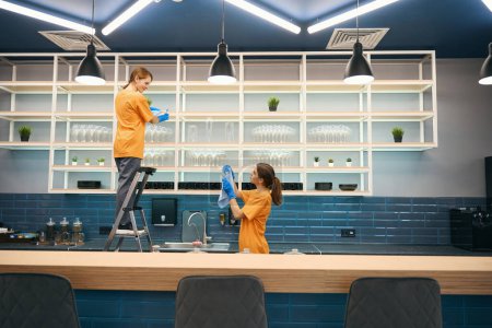 Téléchargez les photos : Employés mignons entreprise de nettoyage communiquent pendant le processus de nettoyage général dans la zone de cuisine dans l'espace de coworking, ils sont en uniformes confortables - en image libre de droit