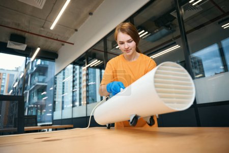 Téléchargez les photos : Femme installe un générateur d'ozone sur un bureau pour purifier l'air dans une zone de coworking - en image libre de droit