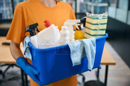 Téléchargez les photos : Nettoyant entreprise de nettoyage tient dans ses mains ensemble professionnel de gadgets pour le nettoyage et la désinfection seau, éponges, spray, serviettes, détergents - en image libre de droit