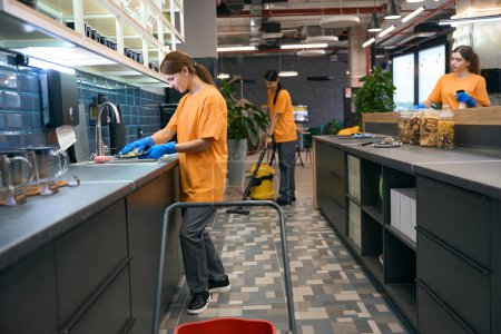 Photo for Team of young women doing cleaning in the kitchen area of a coworking space, they use professional devices - Royalty Free Image