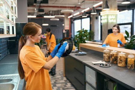 Téléchargez les photos : Nettoyage équipe femme nettoyage dans la zone de cuisine du coworking, les femmes en vêtements de travail et gants de protection - en image libre de droit