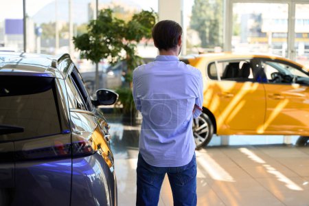 Photo for Back view of buyer standing among brand new motor vehicles at auto dealership - Royalty Free Image