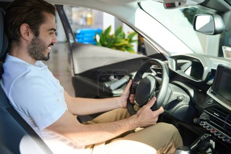Téléchargez les photos : Sourire heureux concessionnaire automobile client assis au volant de la voiture particulière - en image libre de droit