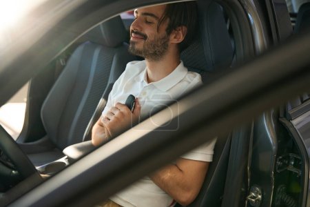 Téléchargez les photos : Agréable gars assis dans le siège conducteur de la voiture de tourisme avec porte-clés automatique dans les mains - en image libre de droit