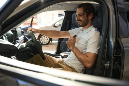 Téléchargez les photos : Joyeux gars avec clé de voiture fob assis dans l'automobile et tourner le volant - en image libre de droit
