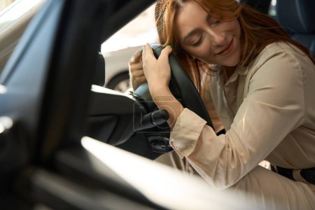 Téléchargez les photos : Souriante joyeuse conductrice embrassant le volant de son nouveau véhicule à moteur - en image libre de droit