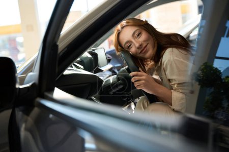 Téléchargez les photos : Sourire satisfait jeune concessionnaire automobile client embrassant volant de son véhicule - en image libre de droit