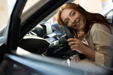Téléchargez les photos : Souriant joyeux jeune femme caucasienne couché dans l'automobile et câlin volant - en image libre de droit